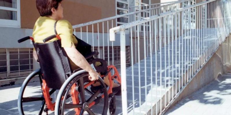 Una mujer en silla de ruedas accede al portal de un edificio de viviendas.