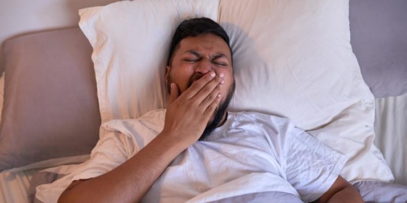 Un hombre bosteza mientras intenta dormir 