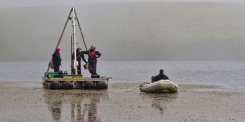 Toma de muestras en el lago Lomba, donde se aprecia el crecimiento de plantas en la superficie