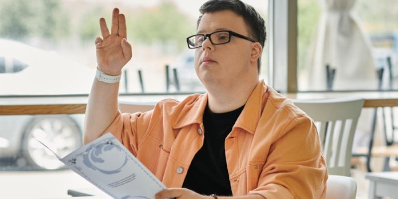 Un joven con síndrome de Down en un restaurante levanta la mano 