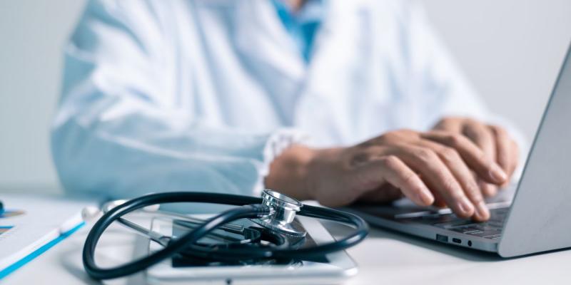 Un médico equipado con un estetoscopio escribiendo en un ordenador 