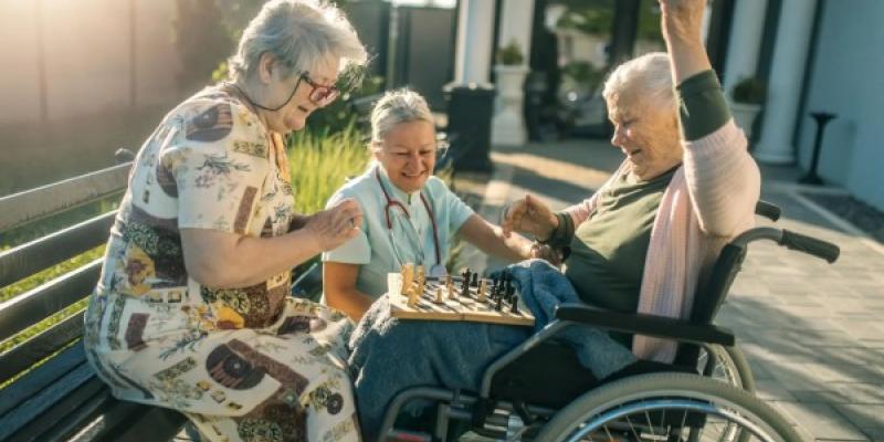 Un grupo de mujeres mayores juegan al ajedrez con su cuidadora