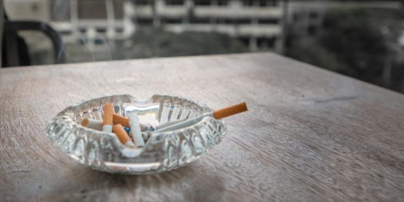 Un cenicero con un cigarrillo humeante en una mesa de una terraza