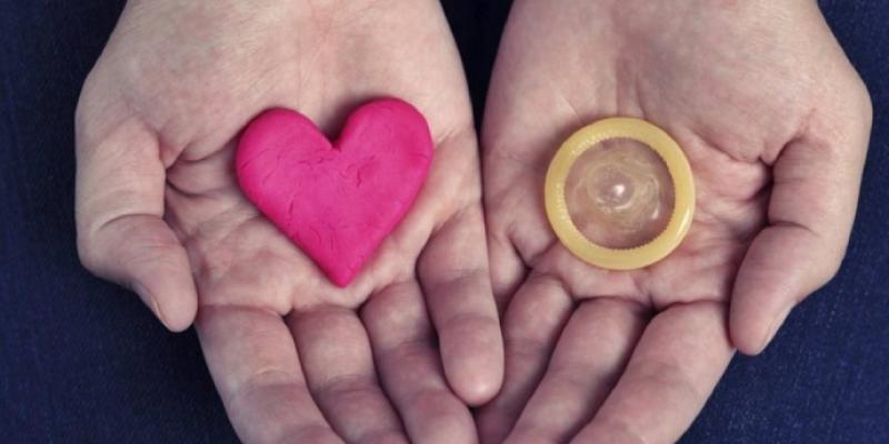 Una mano sostiene un corazón que simboliza la salud y en la otra un preservativo