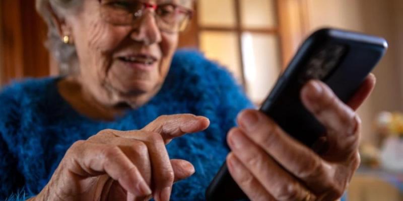Una mujer de avanzada edad utiliza un teléfono móvil mientras sonríe