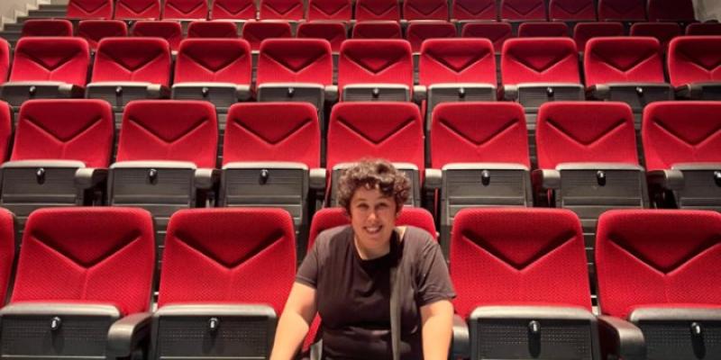 Participante en el proyecto Cerca y Fácil sentada en un patio de butacas rojas vacías 