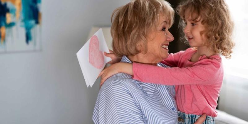 Una abuela abraza a su nieta mientras esta sostiene un dibujo para ella 