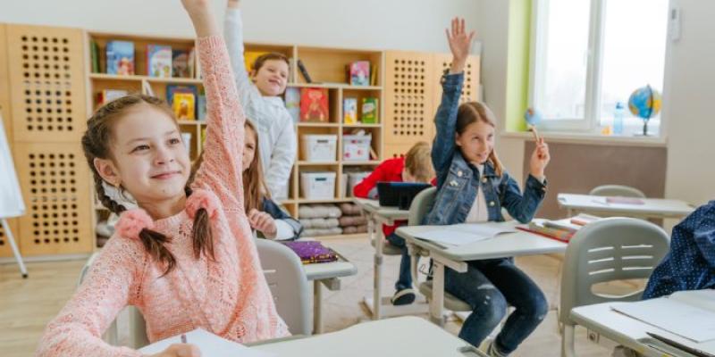 Una niña en el aula de clase levantando la mano 