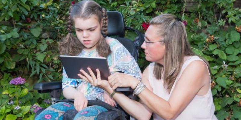 Madre con su hija en silla de ruedas leyendo en una tablet