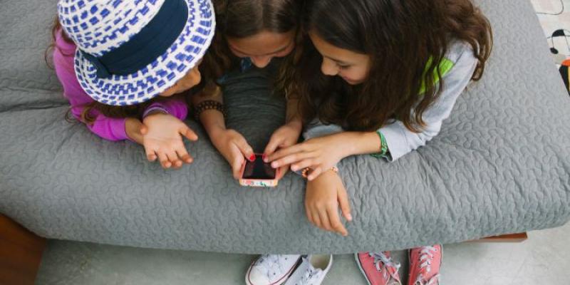 Tres niñas consultan un teléfono móvil 