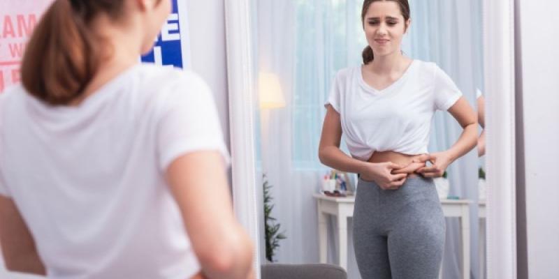 Mujer frente al espejo sufriendo por la violencia estética