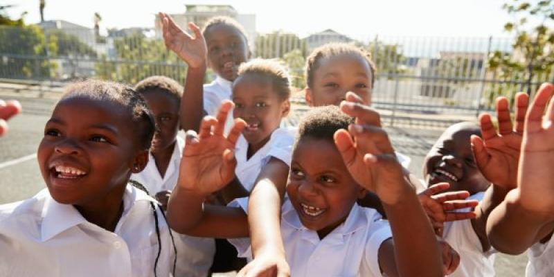 Niños de primaria en el patio de recreo saludando a la cámara