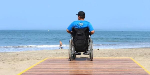 Hombre con silla de ruedas accediendo a una playa 