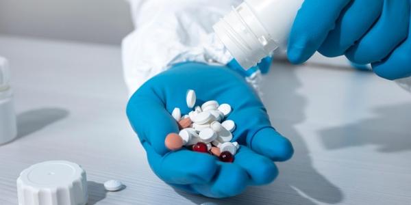 Mano de un sanitario con guantes azules sosteniendo un puñado de pastillas de colores