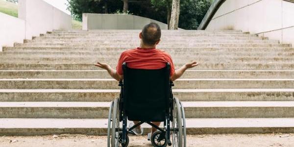 Hombre en silla de ruedas indignado frente a las escaleras. 