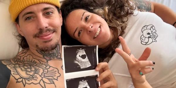 Bruno León y su pareja tumbados en la cama enseñando una ecografía de su bebé