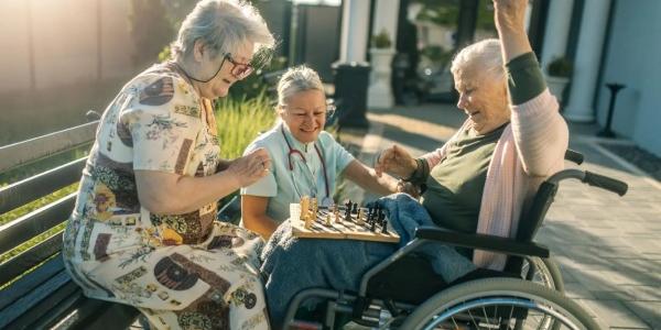 Un grupo de mujeres mayores juegan al ajedrez con su cuidadora