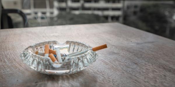 Un cenicero con un cigarrillo humeante en una mesa de una terraza