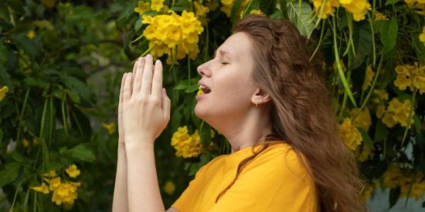 Una mujer estornuda tocando unas flores 