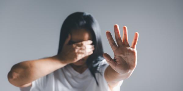 Una mujer tapa su cara con una mano y estira la otra en señal de freno 