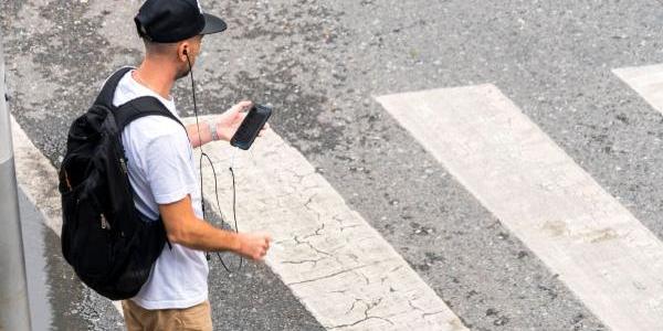 Chico mirando su teléfono antes de cruzar por un paso de peatones