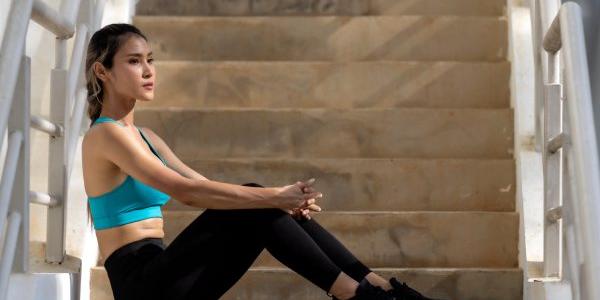 Una mujer asiática con ropa de ejercicio se sienta en las escaleras, abatida. Fatiga después del ejercicio, depresión femenina, contaminación mental