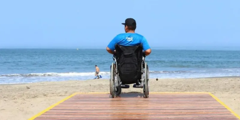 Hombre con silla de ruedas accediendo a una playa 