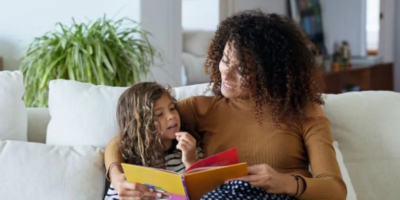 Madre con una hija en el sofá leyendo un cuento