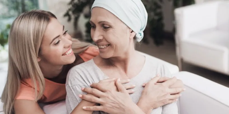 Una mujer con cáncer está sentada en un sofá blanco al lado de su hija 