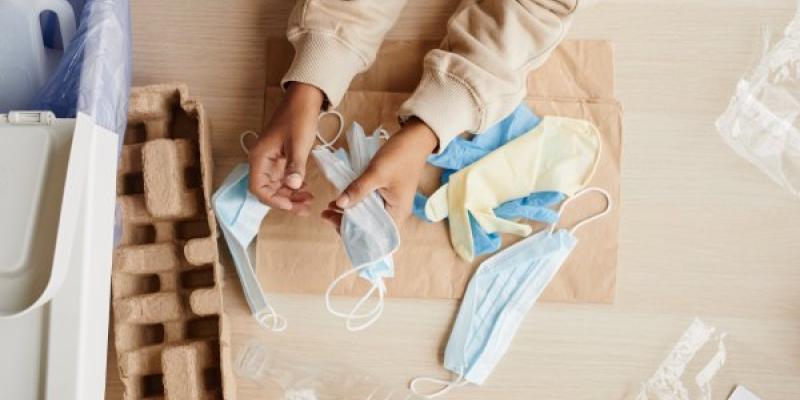 Vista desde arriba, primer plano de un niño afroamericano que prepara la basura doméstica para su reciclaje, guantes y máscaras