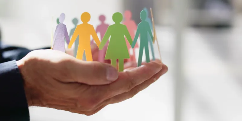 Manos de una persona sosteniendo un grupo diverso de personas en cartulina