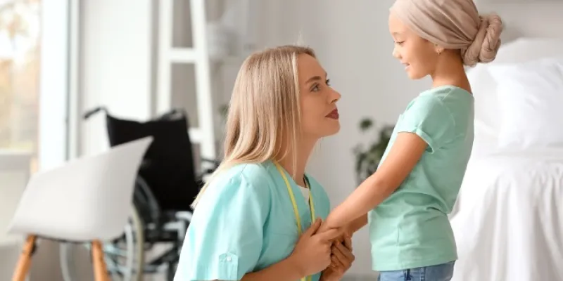 Una profesional sanitaria coge las manos a un niño con cáncer