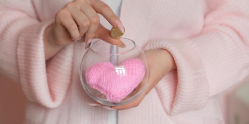 Mano de una chica guardando dinero en una hucha con corazón