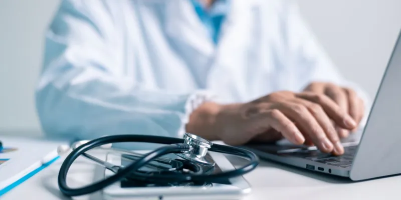 Un médico equipado con un estetoscopio escribiendo en un ordenador 