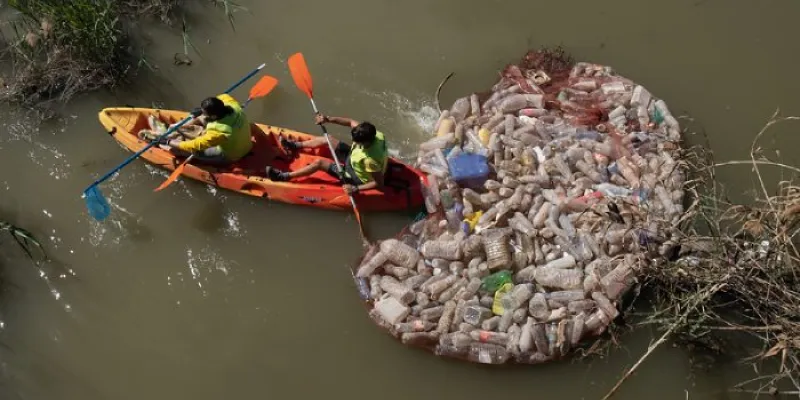 Dos operarios retiran envases de un lugar fluvial