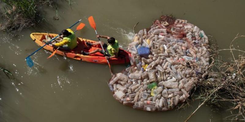 Dos operarios retiran envases de un lugar fluvial