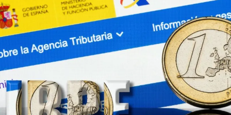 Imagen de una moneda de euro sobre un fondo donde se ve la página web de la Agencia Tributaria