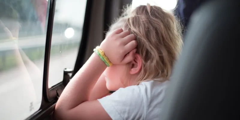 Una niña con las manos en la cara mira por la ventanilla del coche 