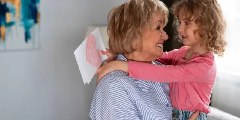 Una abuela abraza a su nieta mientras esta sostiene un dibujo para ella 