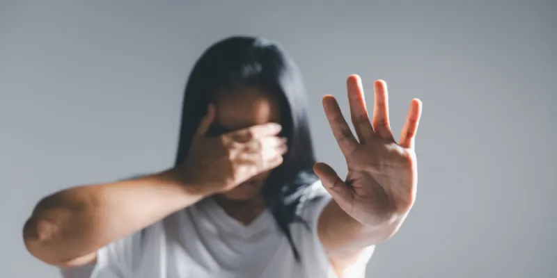 Una mujer tapa su cara con una mano y estira la otra en señal de freno 
