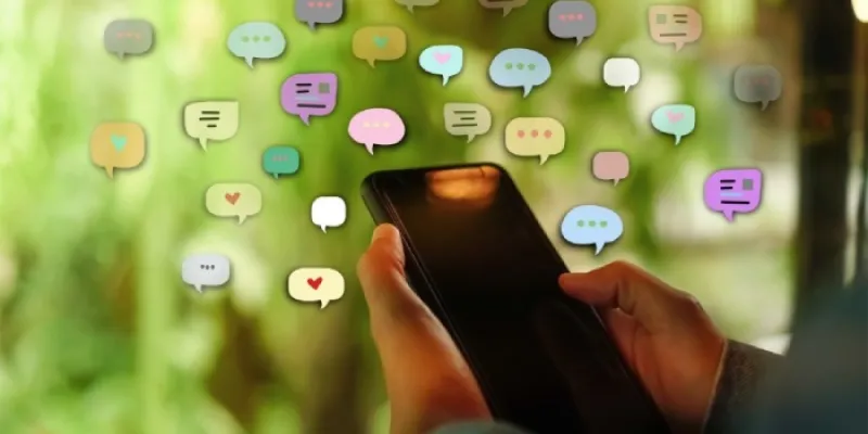 Una persona sostiene en la mano un teléfono, rodeado de representaciones de mensajes de redes sociales 