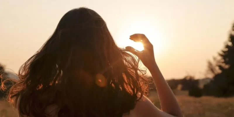 Una mujer observa el sol poniendo su mano como una visera