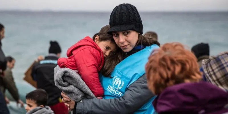 Una trabajadora de ACNUR sostiene en brazos a un niño refugiado envuelto en una manta. La embarcación en la que viajaba la criatura llegó a Lesvos, una isla griega.  