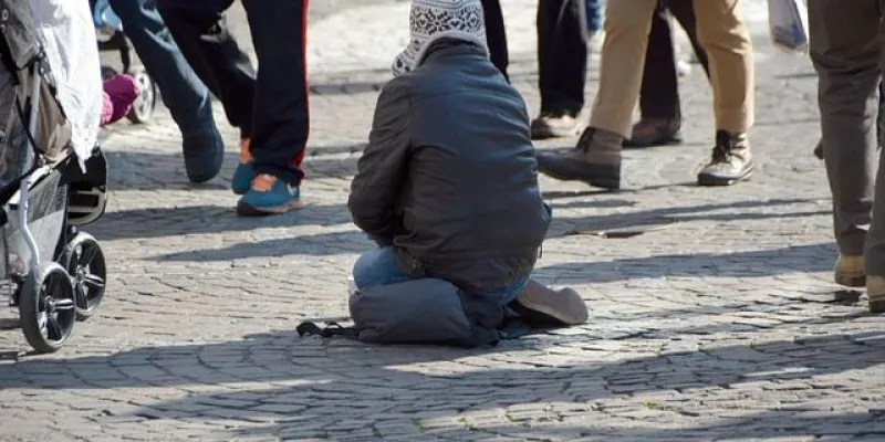 Persona sin recursos arrodillada en la calle pidiendo dinero