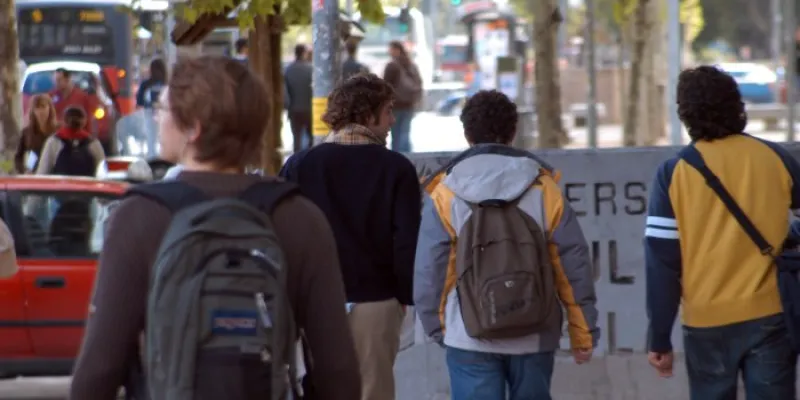 Grupo de personas caminando por una acera en una zona urbana cerca de una universidad