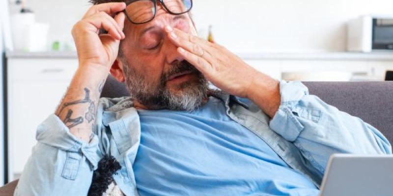 Empresario cansado se quita las gafas y siente fatiga visual por trabajar en línea con una computadora portátil, un hombre caucásico se sienta en el sofá y se frota los ojos, siente dolor de cabeza y falta de energía