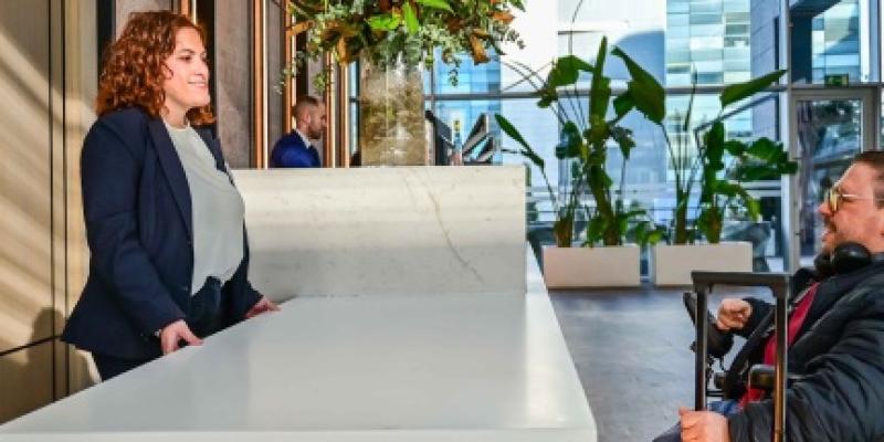 Recepción de un establecimiento de turismo accesible atendiendo a una persona en silla de ruedas