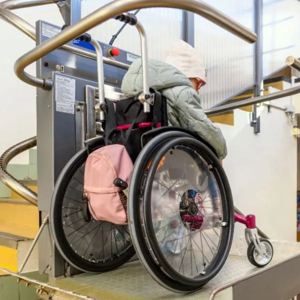 Mujer con discapacidad en silla de ruedas bajando las escaleras por un elevador adaptado