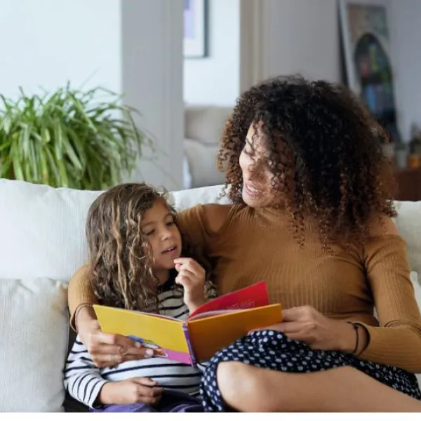Madre con una hija en el sofá leyendo un cuento