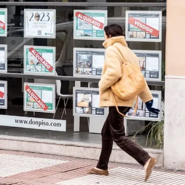 Una joven camina ante el escaparate de una agencia inmobiliaria